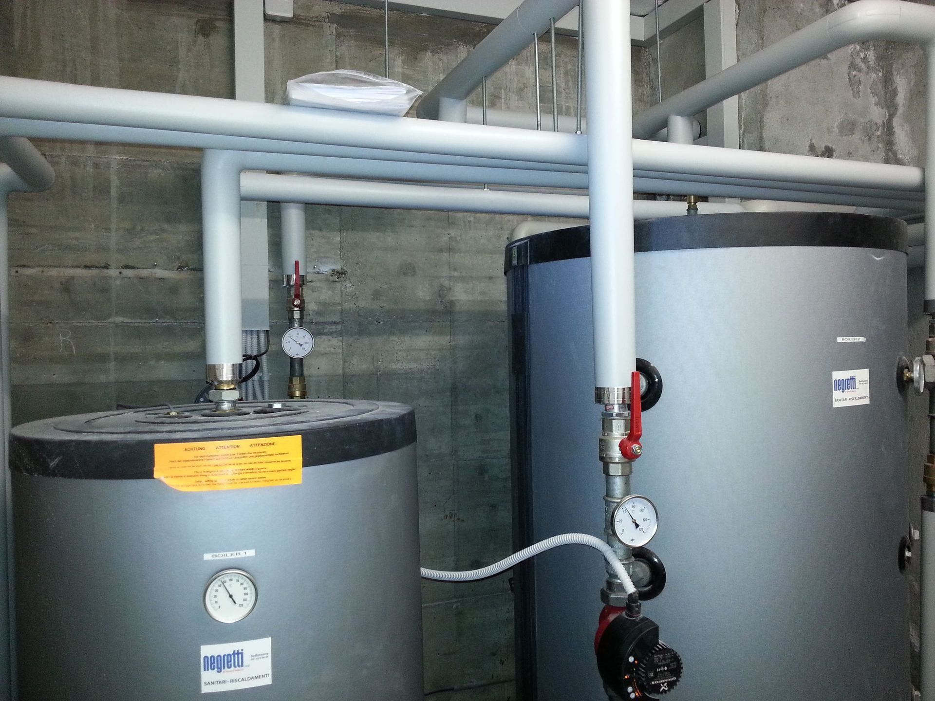 Due serbatoi cilindrici grigi per l'acqua con tubi e manometri collegati in un ripostiglio.