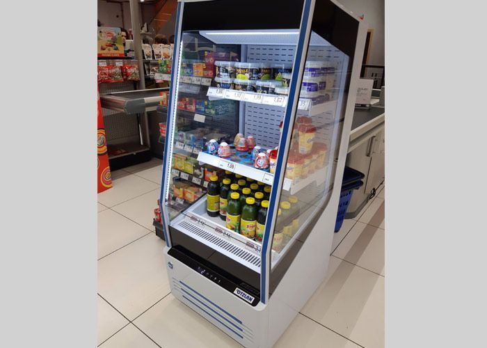 Un refrigerador lleno de botellas de refresco y otros artículos en una tienda.