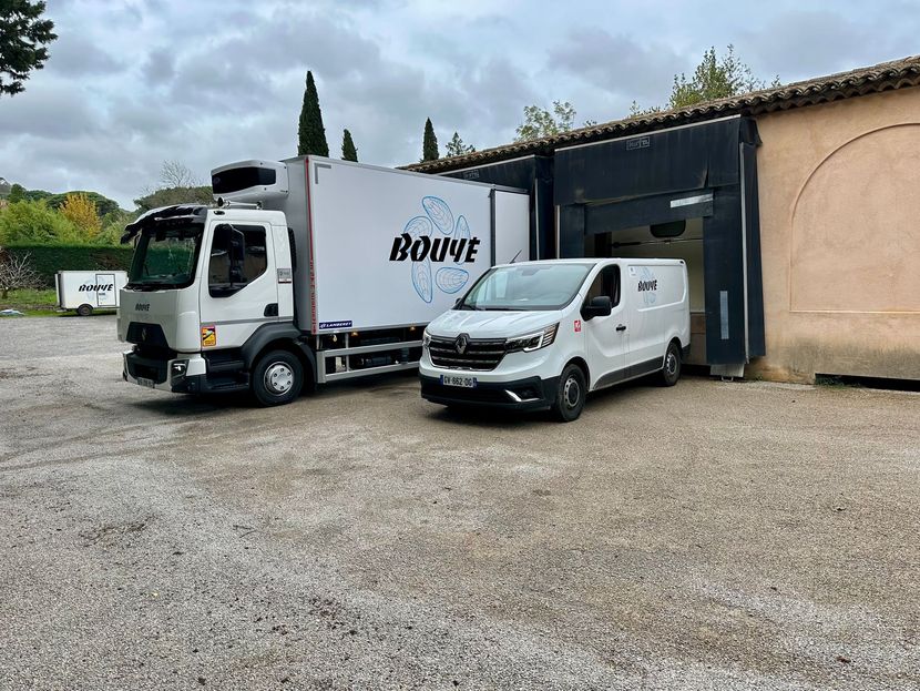 Un camion de livraison blanc et une camionnette sont stationnés devant un entrepôt, tous deux portant le logo BOUYÉ.
