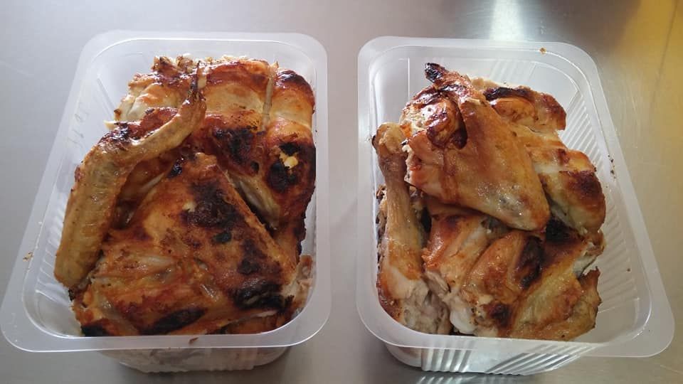 Dos recipientes de plástico llenos de alitas de pollo están sobre una mesa.