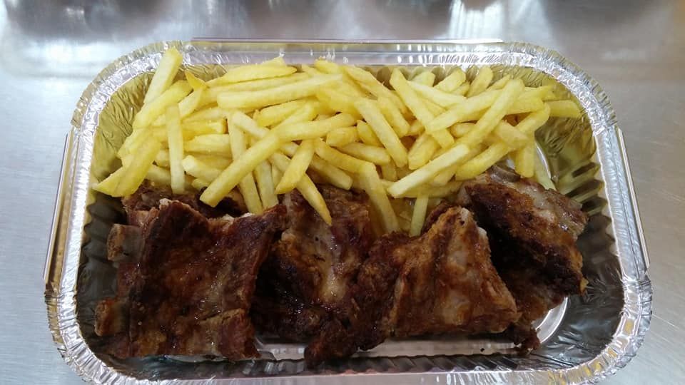 Bandeja de papel de aluminio llena de costillas y papas fritas sobre una mesa.