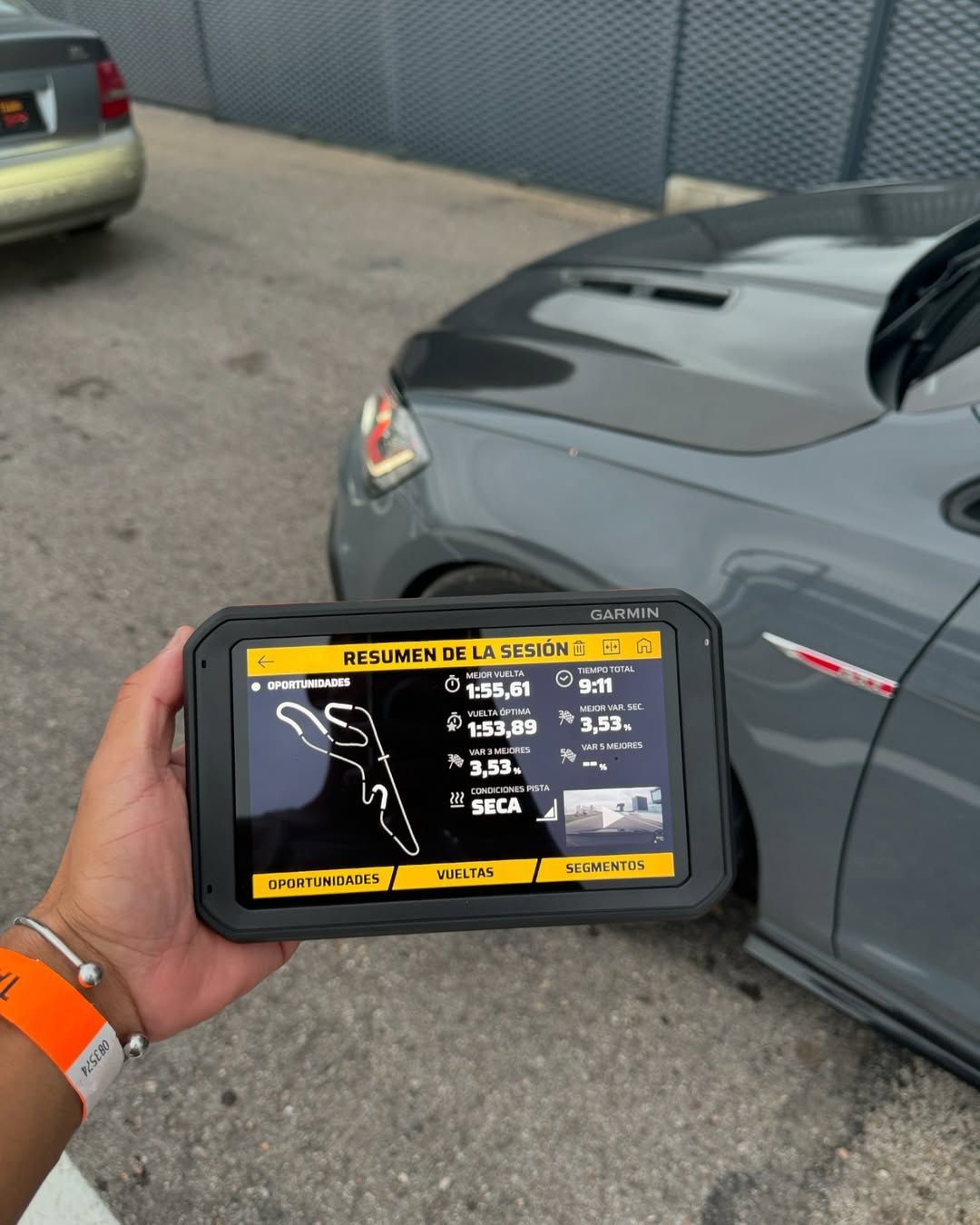 Una persona sostiene una tableta delante de un coche gris.