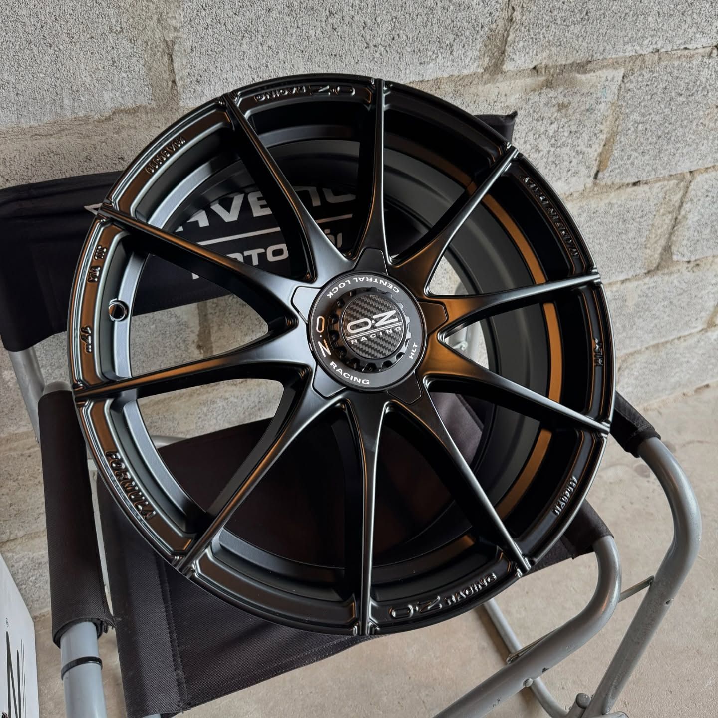 Una rueda negra reposa sobre una silla plegable frente a una pared de ladrillos.