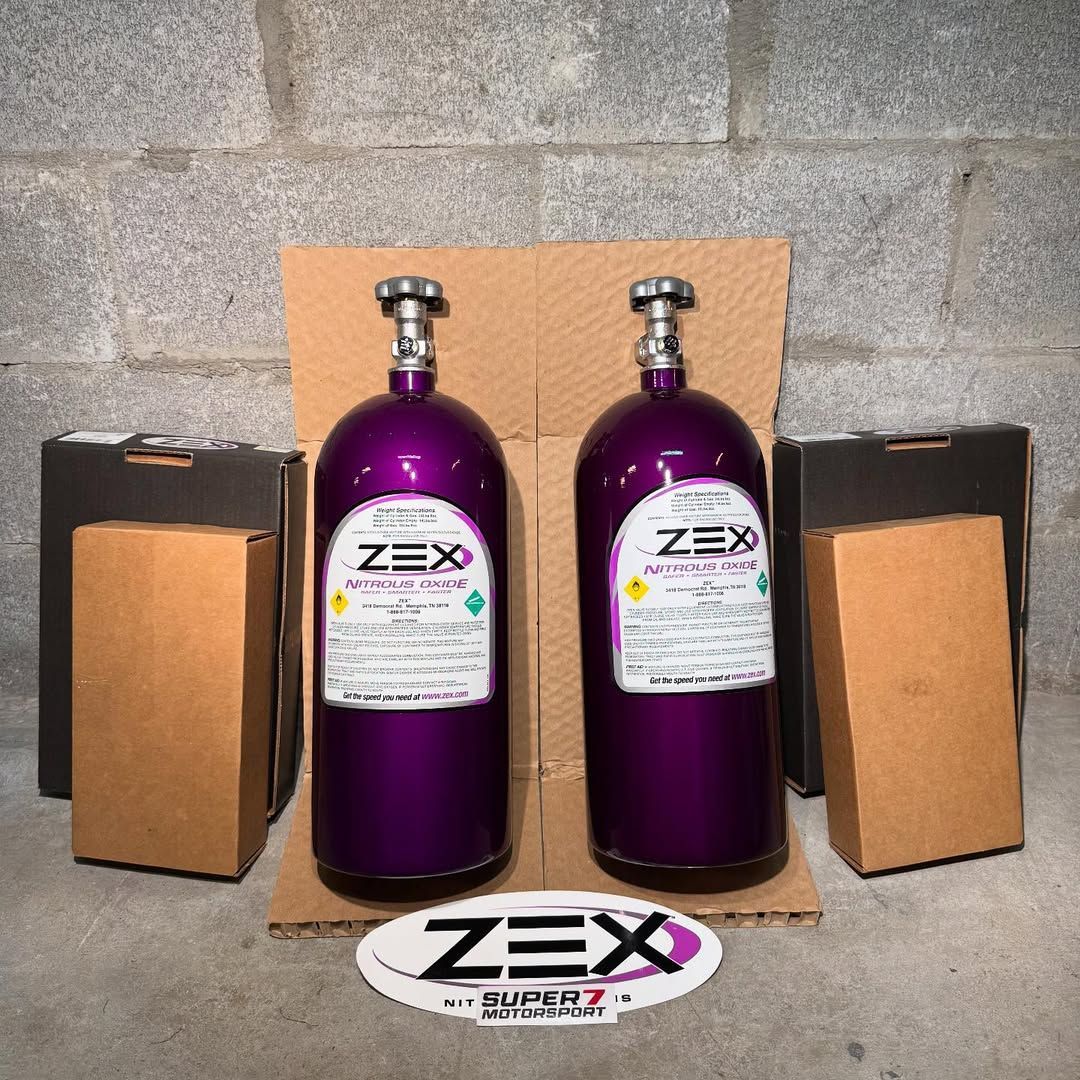 Dos botellas moradas de Zex están sobre una caja de cartón.