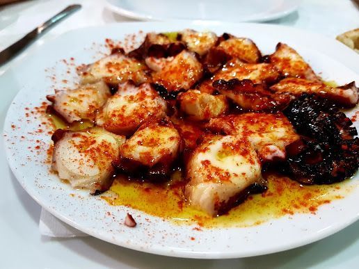 Un plato blanco cubierto con pulpo y salsa sobre una mesa.