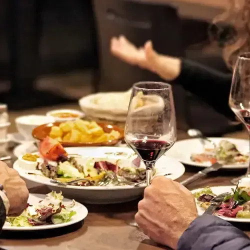 Un grupo de personas está sentado en una mesa con platos de comida y copas de vino.