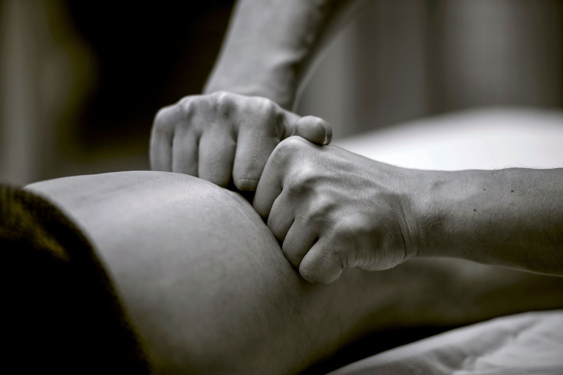 Des mains massent la jambe d'une personne dans une scène en gros plan en noir et blanc.