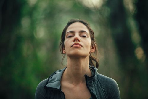 Une femme détendue les yeux fermés dans la forêt.