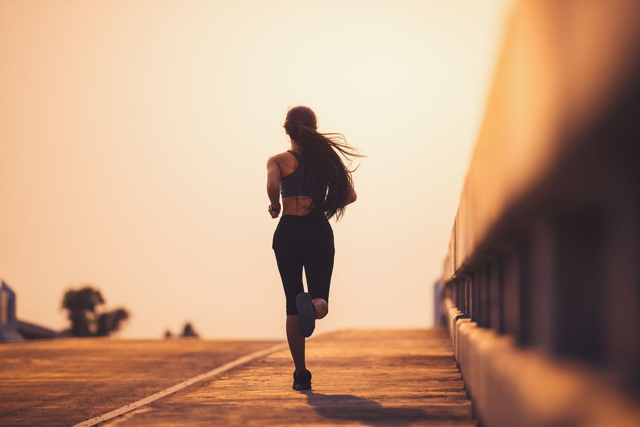 Une coureuse fait son jogging sur un chemin ensoleillé au coucher du soleil.