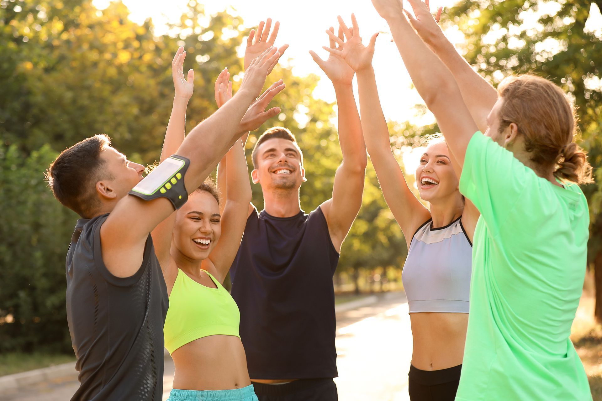 Un groupe de personnes se tapent dans la main en plein air, tout sourire, vêtues de tenues de sport.