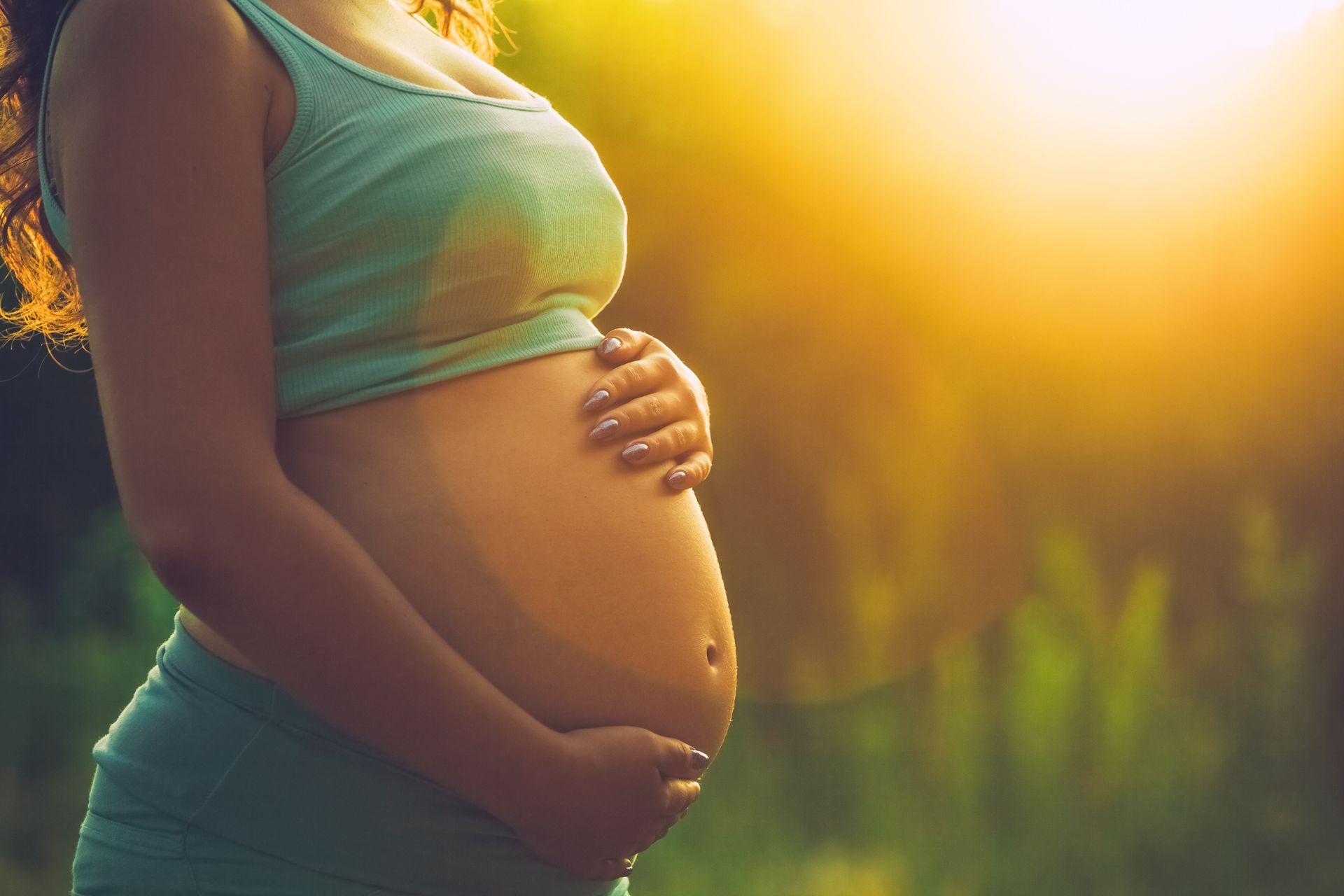 Une femme enceinte avec les deux mains posées sur son ventre, debout en extérieur