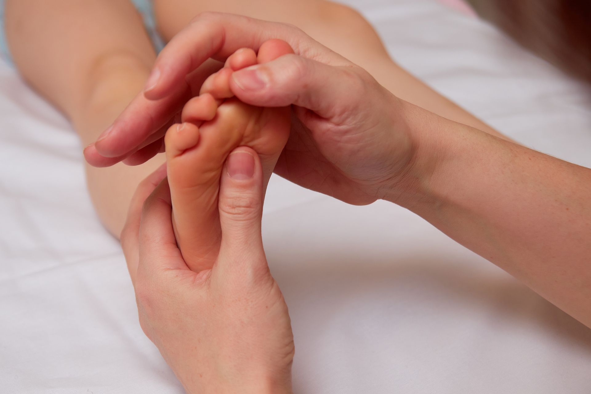 Une main d'adulte tenant délicatement le pied d'un bébé lors d'une séance de soin.