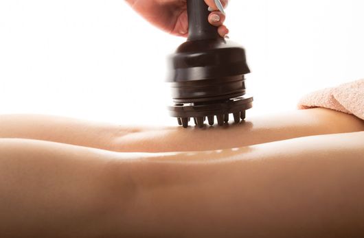 Outil de massage manuel appliqué sur des jambes sur une table de soin.