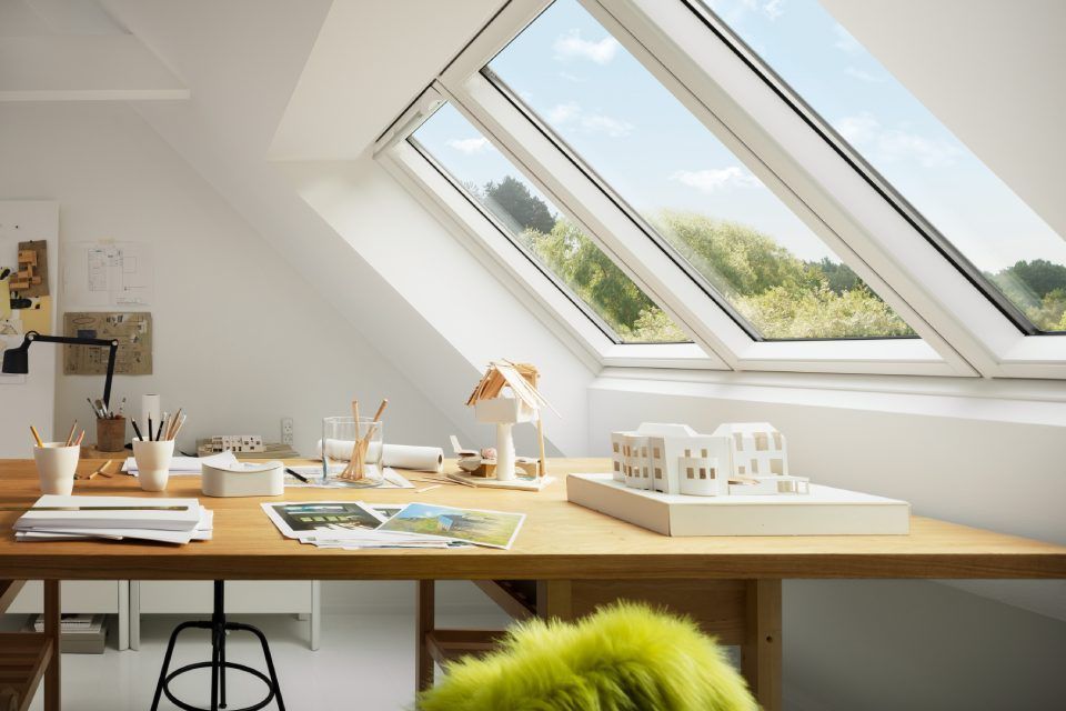 Ein lichtdurchfluteter Arbeitsbereich mit einem großen Holzschreibtisch, einem Model und schrägen Oberlichtern mit Aussicht.