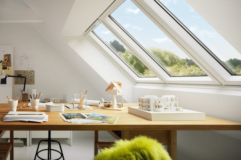 Ein lichtdurchfluteter Arbeitsbereich mit einem großen Holzschreibtisch, einem Model und schrägen Oberlichtern mit Aussicht.