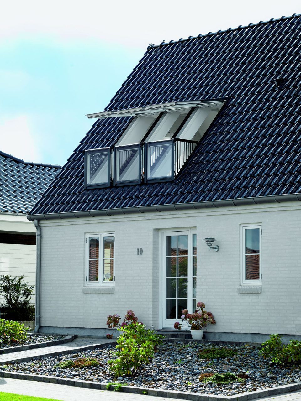 Ein weißes Backsteinhaus mit dunklem Ziegeldach und einem Balkon mit drei Glastüren im Dachgeschoss.