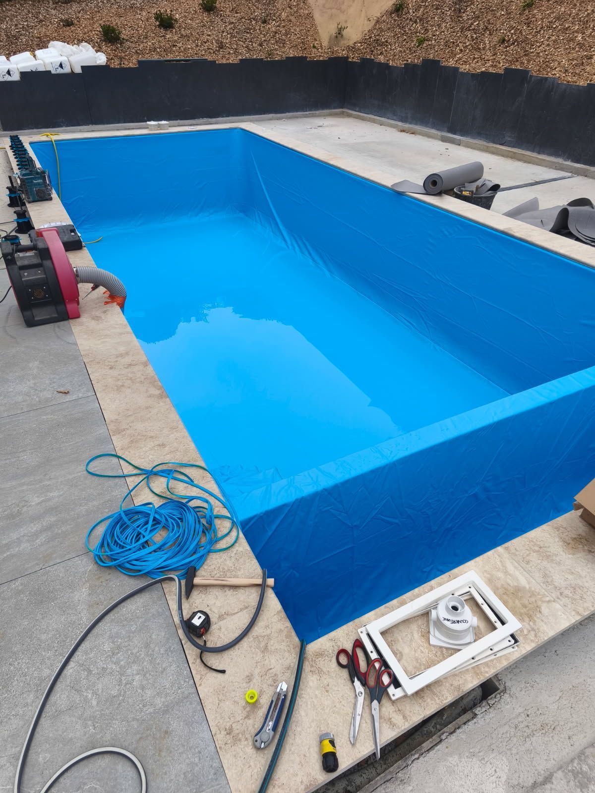 Piscine rectangulaire en construction, délimitée par des lignes bleues ; outils et équipements sur le béton environnant.