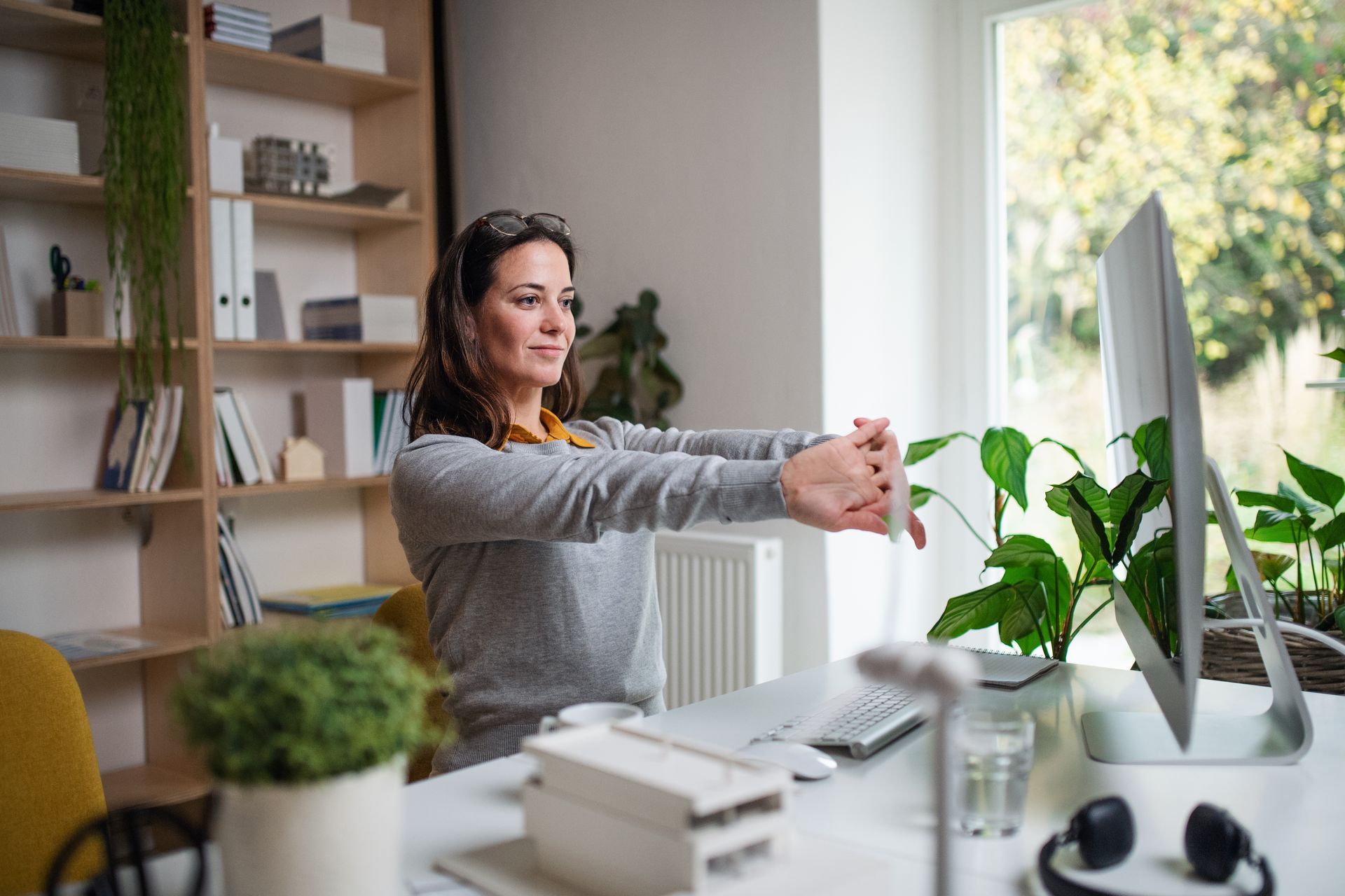 Une femme étire les bras devant un bureau équipé d'un ordinateur, dans un bureau à domicile.