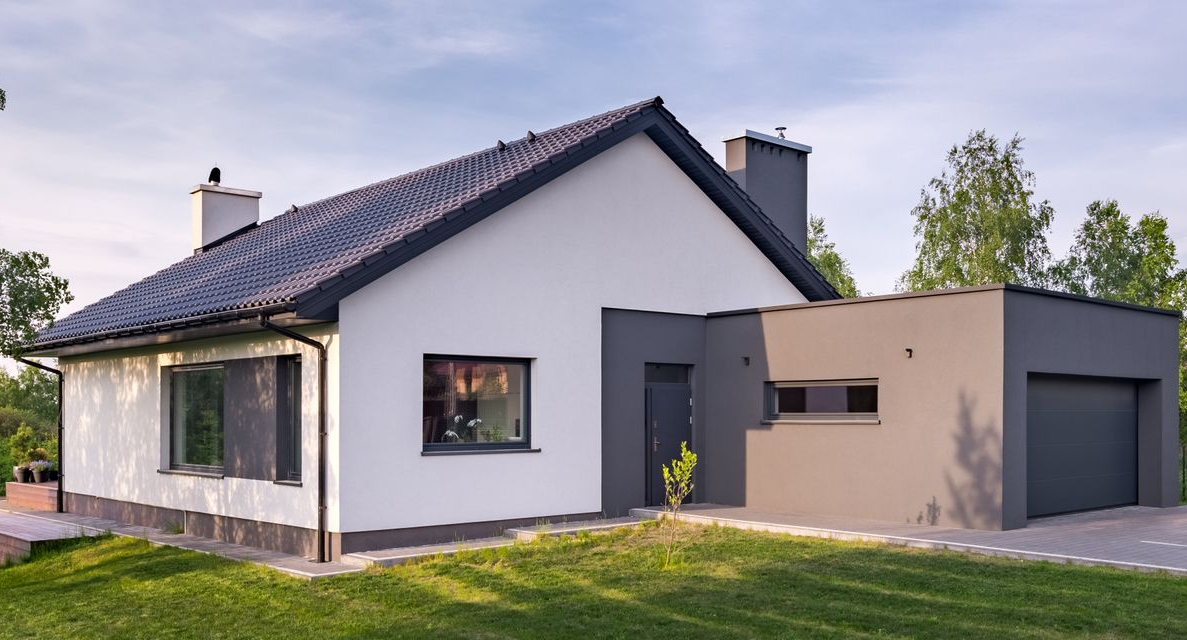 Maison moderne blanche et grise avec toit noir, garage et pelouse verte.