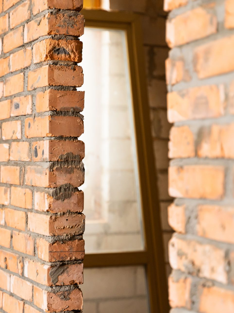 Gros plan sur un mur de briques avec une porte ouverte donnant sur une fenêtre en arrière-plan.