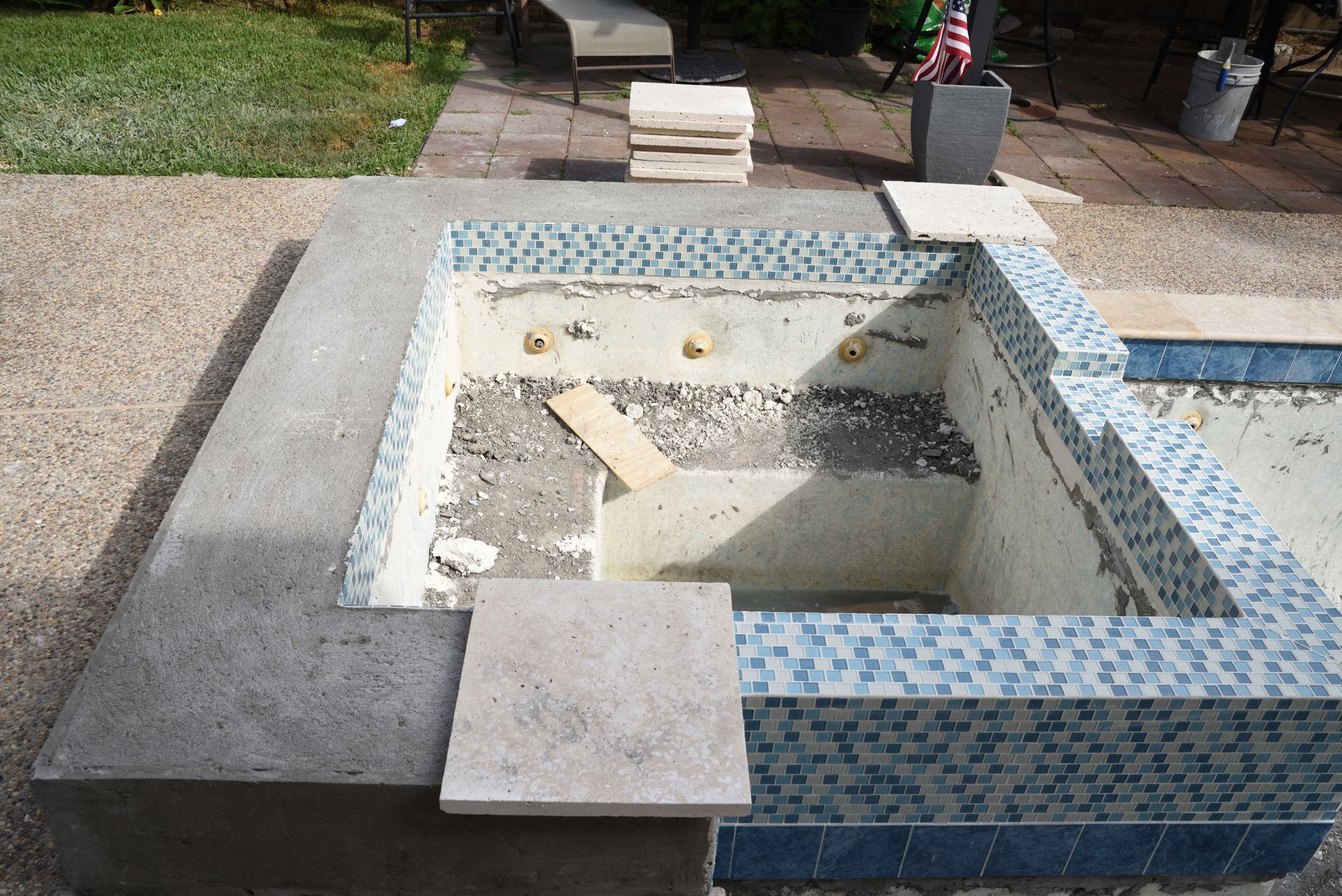 Piscine avec carrelage partiellement enlevé, contour en béton et mosaïque bleue.