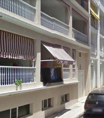 Fachada de un edificio de apartamentos con toldos a rayas y un coche aparcado en una calle estrecha