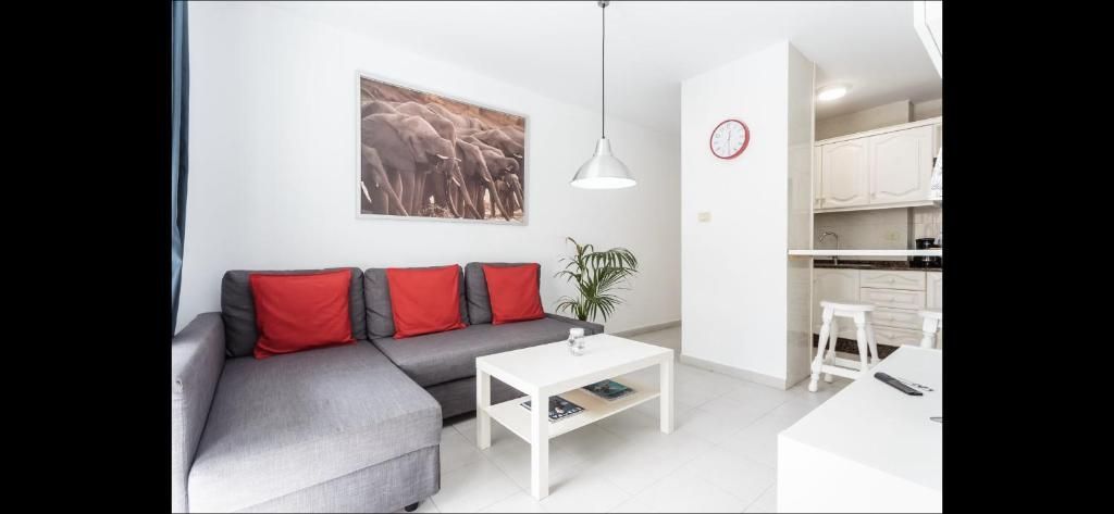 Luminoso y moderno salón con sofá gris, cojines rojos, mesa de centro blanca y cuadros en la pared