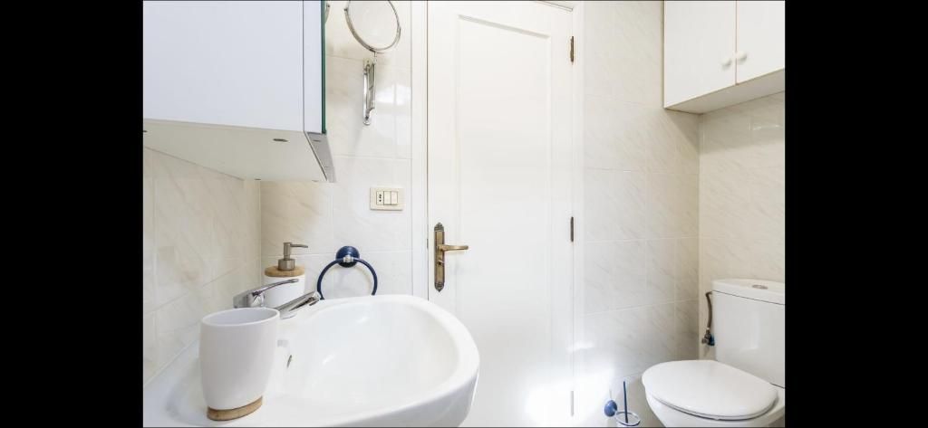 Cuarto de baño pequeño y blanco con lavabo, inodoro, espejo y armarios de pared.