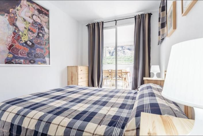 Dormitorio luminoso con una colcha de cuadros, una ventana con cortinas grises y arte colorido en las paredes