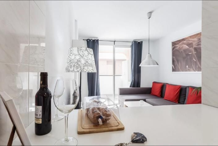 Salón moderno blanco con cojines rojos, sofá, mesa de centro, botella de vino y lámpara decorativa