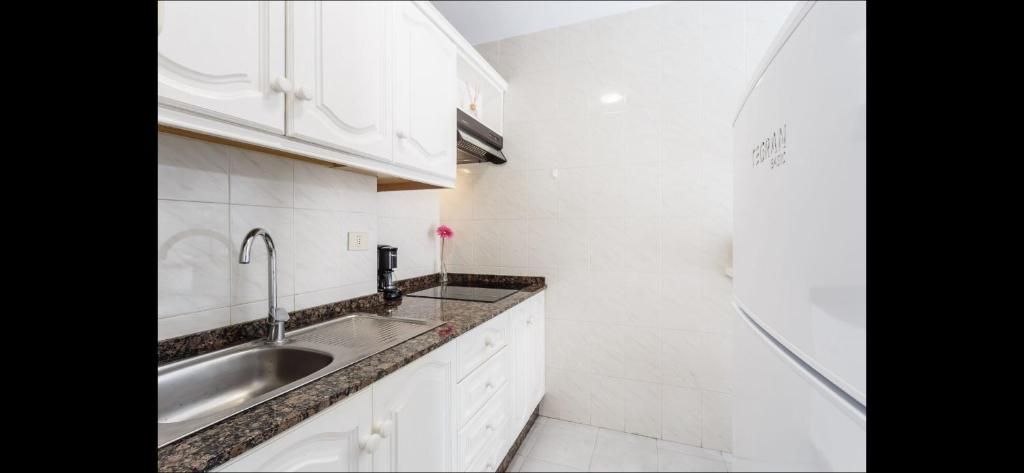 Cocina de un blanco luminoso con encimeras de granito negro, armarios blancos, fregadero y refrigerador integrado.