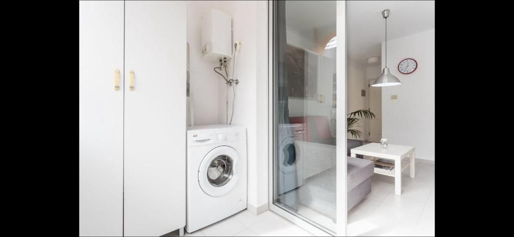 Baño luminoso con lavadora, ducha de cristal, armarios blancos y una mesita con lámpara