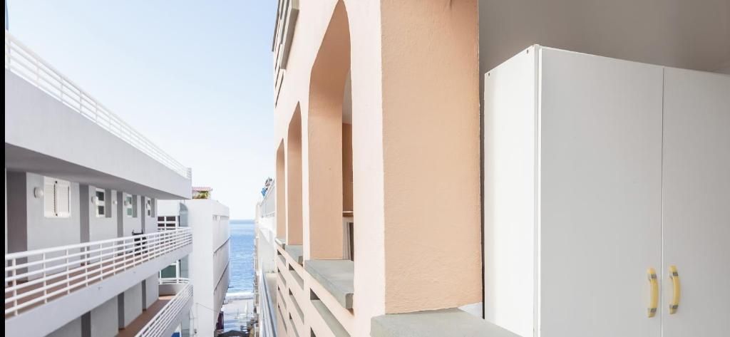 Vista estrecha entre edificios de apartamentos con balcones y barandillas blancas, que deja ver un pasaje hacia el mar al fondo