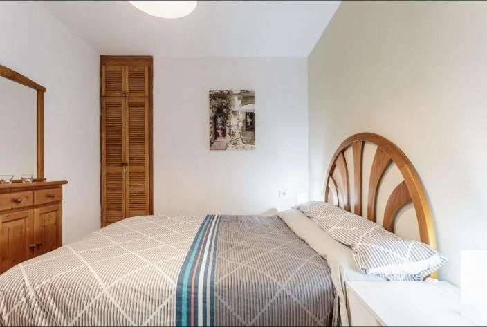 Dormitorio luminoso con una cama, una cómoda de madera, la puerta de un armario y paredes blancas