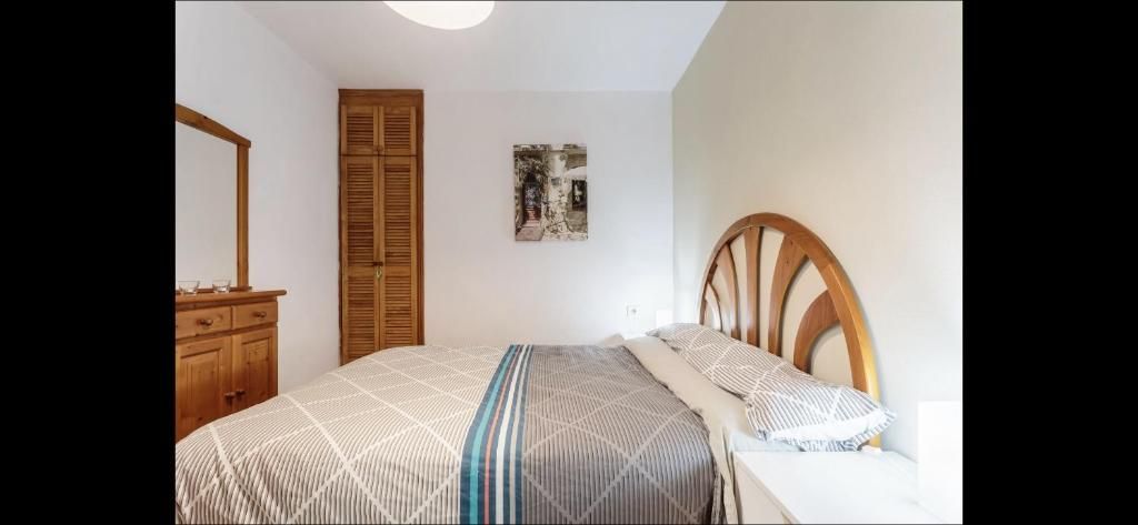 Dormitorio luminoso con una cama de madera, una cómoda, un armario cerrado y paredes blancas.