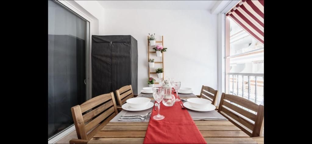 Conjunto de comedor en un balcón luminoso con camino de mesa rojo, sillas de madera y toldo a rayas.