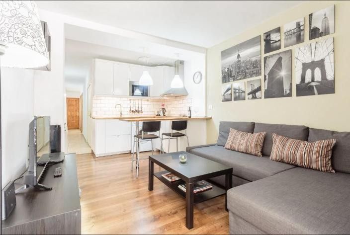 Sala de estar moderna con sofá seccional gris, mesa de centro, televisor y cocina abierta con taburetes de bar