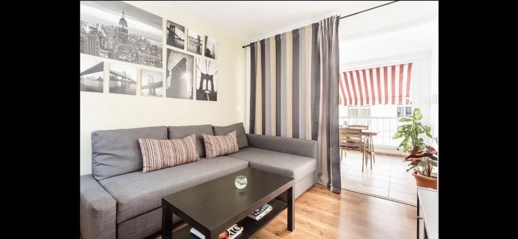 Salón moderno con sofá gris, mesa de centro, cuadros y cortinas a rayas que dan a un balcón