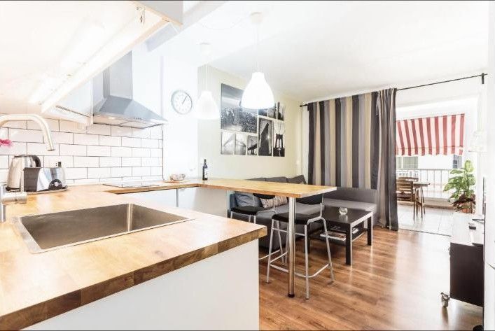 Cocina y comedor luminosos y modernos, con suelos de madera, armarios blancos y cortinas de rayas en el balcón