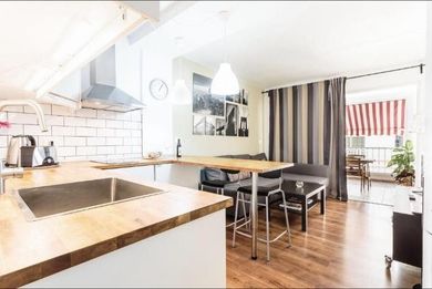 Cocina y comedor luminosos y modernos, con suelos de madera, armarios blancos y cortinas de rayas en el balcón