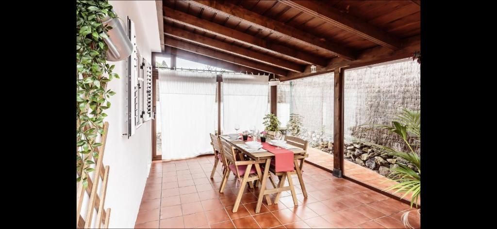 Patio cubierto con suelo de terracota, vigas de madera en el techo, una mesa y sillas junto a un muro del jardín.