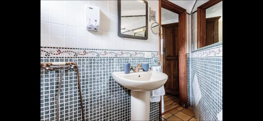 Baño pequeño con paredes de mosaico, lavabo con pedestal, espejo y puerta de madera.