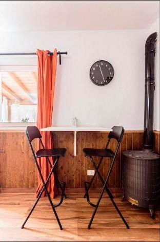 Dos taburetes altos junto a una mesita redonda en una acogedora habitación con un reloj de pared y cortinas naranjas