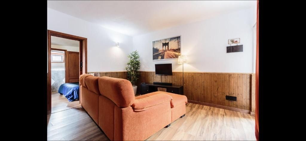 Acogedor salón con sofá color melocotón, televisor, pared revestida de madera y una puerta abierta a otra habitación