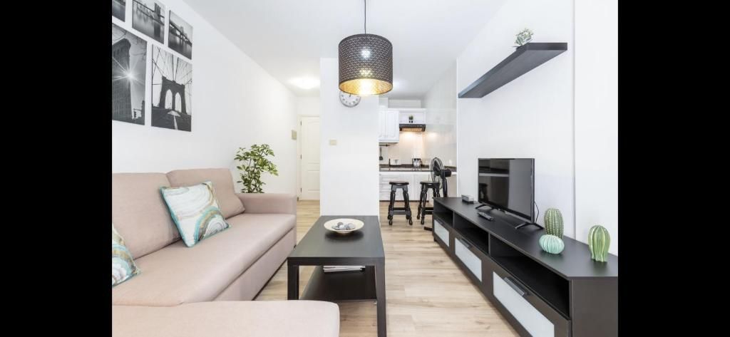 Sala de estar luminosa y moderna, con un sofá beige, un mueble de TV negro y un comedor al fondo