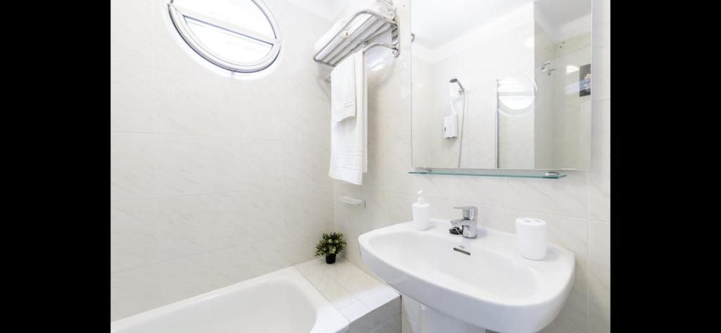 Baño de un blanco luminoso con bañera, lavabo, espejo, toallero y espejo redondo de pared.