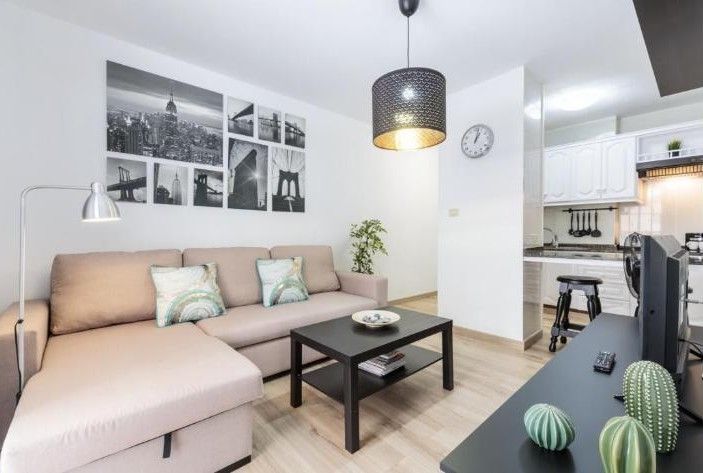 Sala de estar moderna con sofá seccional beige, mesa de centro negra, cuadros en la pared y vistas a la cocina.