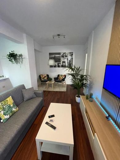 Sala de estar moderna con sofá gris, mesa de centro blanca, cuadros, plantas y un televisor en una pared revestida de madera
