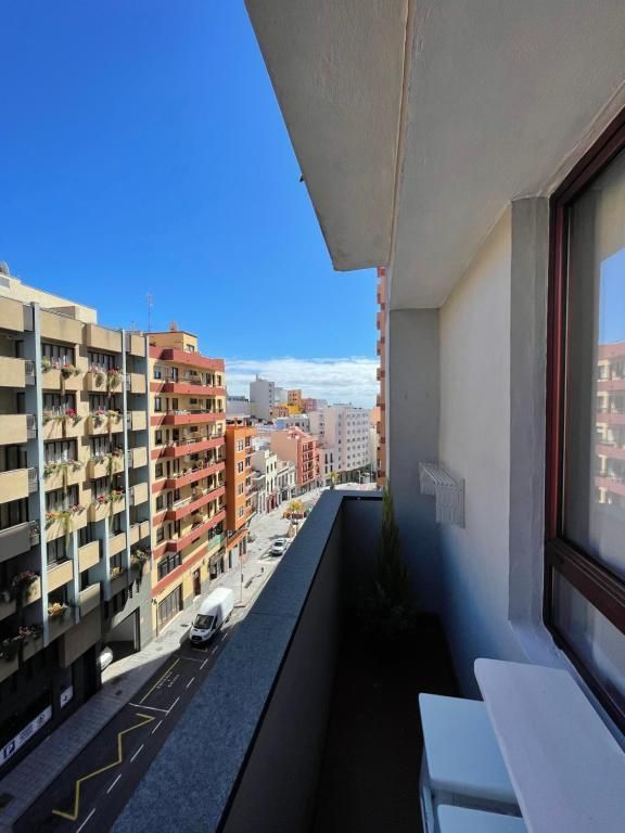 Vista desde un balcón de una calle de la ciudad, con edificios de apartamentos bajo un cielo azul despejado
