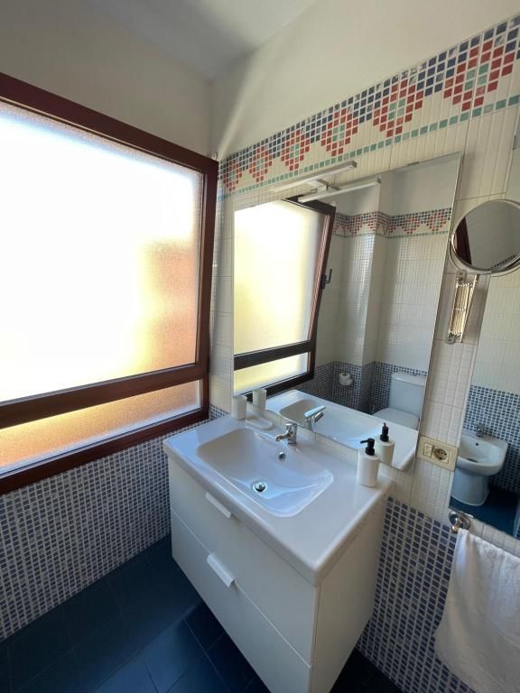 Mueble de baño pequeño con lavabo, espejo, cortina de ducha y detalles de mosaico junto a una ventana luminosa.